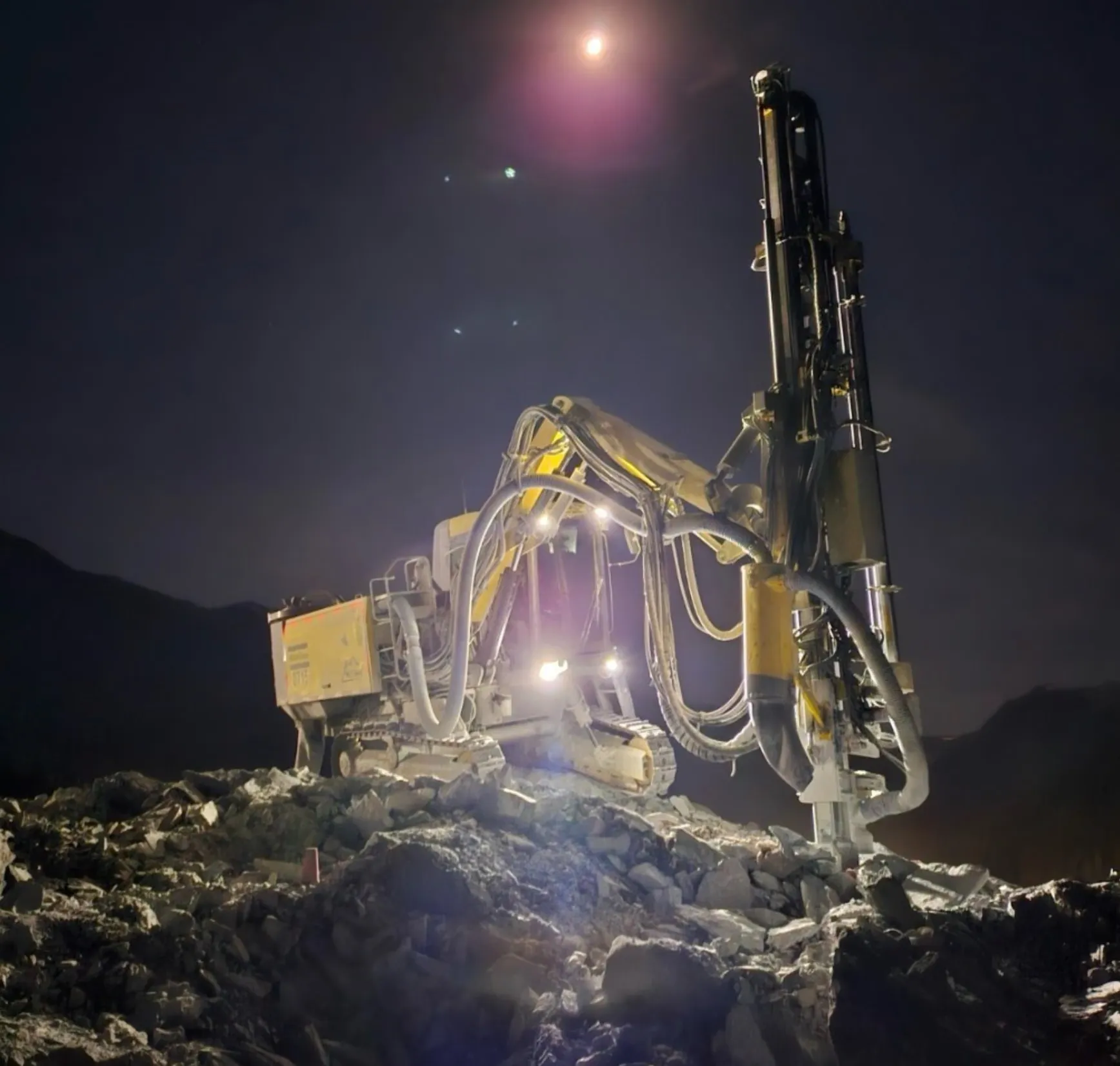 McCaw's drill rig working under lights after dark on a mountain slope